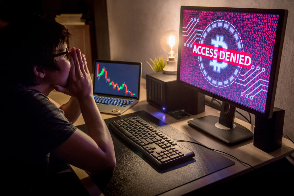 Person reacting to “Access Denied” warning on Bitcoin-themed computer screen after suspected cryptocurrency account breach or crypto scam attack.
